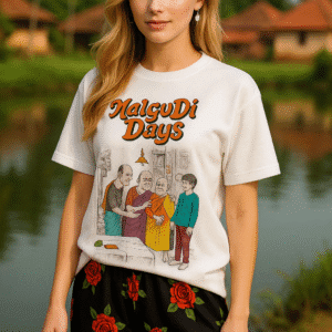 A Tshirt with colorful cartoon-style illustration titled "Malgudi Days" in bold orange letters at the top. The scene depicts four characters in a traditional Indian setting: two older men in the center, one in an orange shirt and green dhoti and the other in a black kurta with a blue dhoti, engaged in a lively interaction with one holding the other's arm. A woman in a yellow saree and a young boy in a blue kurta and red pants stand nearby, observing curiously. The background features a hanging bell, a decorated wall with traditional motifs, and a table with a vegetable and a small box, evoking a mid-20th-century South Indian village atmosphere.